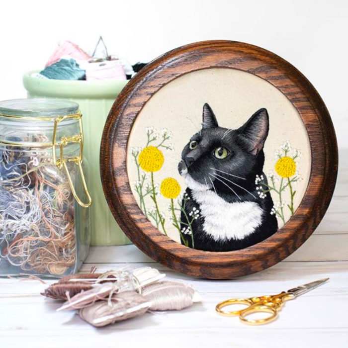 Artista Michelle Staub hace bordados de mascotas; bordado de gato negro con manchas blancas, ojos verdes y flores amarillas