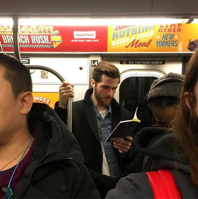 Chico con chamarra negra leyendo en el metro 