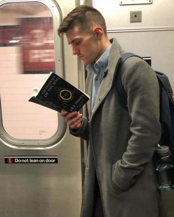 Hombre con gabardina gris y camis a azul leyendo en el metro