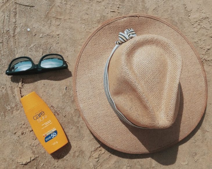 Sombrero de playa, gafas de sol y protector solar en la arena