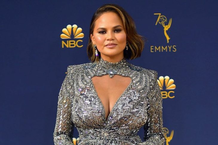 Chrissy Teigen usando un vestido de color plateado con brillos durante la alfombra roja de los EMYS de la cadena NBC