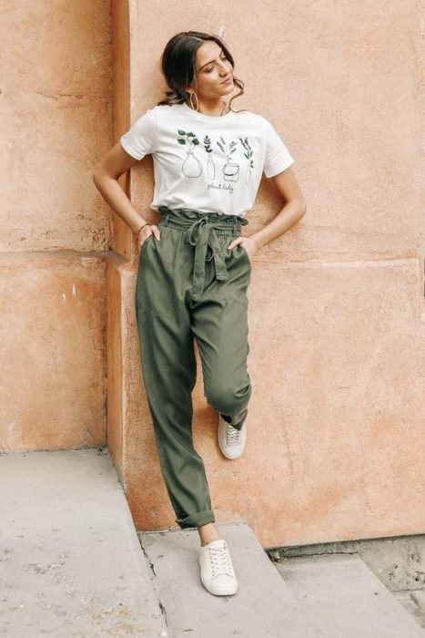 Chica recargada en la pared con baggy pants verdes y blusa blanca