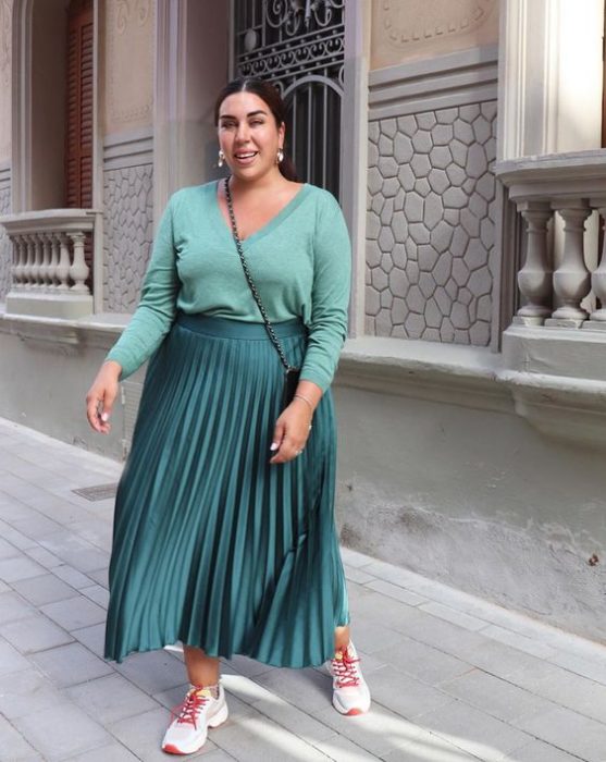 Chica curvy con suéter verde y falda verde metálica con tenis coloridos