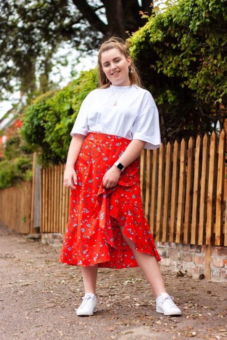 Chica curvy con camisa blanca y falda floreada roja y tenis blancos