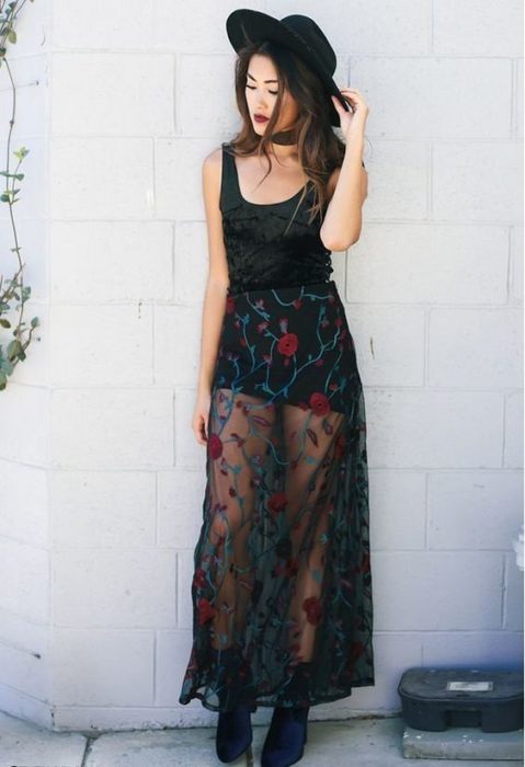 Chica llevando falda cn transparencias en negro con bordado de rosas en tono rojo y blusa negra de tirantes con sombre a juego