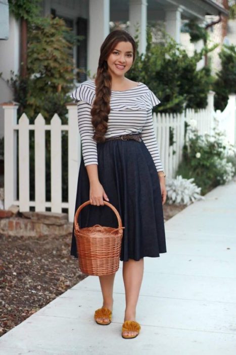 Mujer con blusa de rayas blanco con azuk, falda larga y bolso tipo canasta