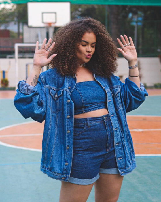 Looks con short vintage; chica morena de cabello chino y esponjado, chamarra y crop top de mezclilla, plus size, en una cancha de basquetbol