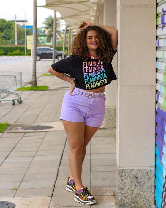 Looks con short vintage; chica morena de cabello chino, largo y esponjado, con blusa feminista y tenis de colores