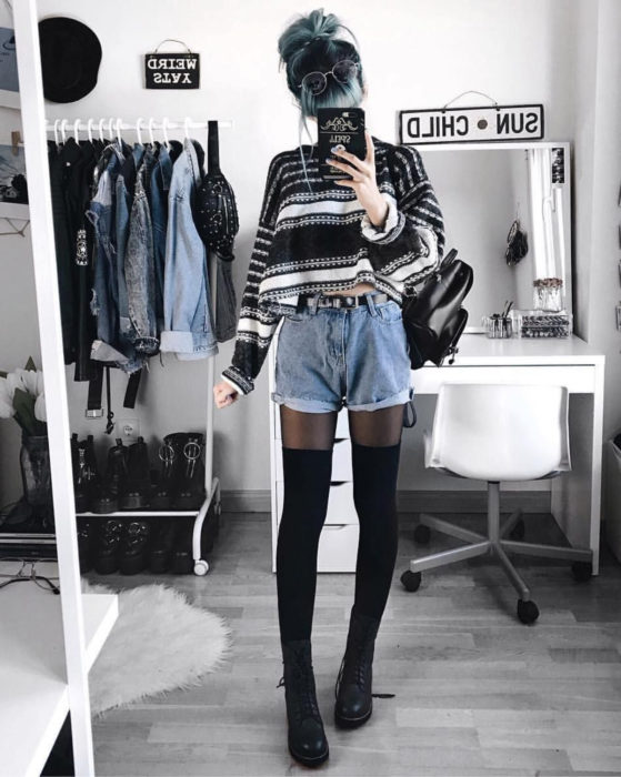 Looks con short vintage;chica tomándose selfie frente al espejo, cabello azul con raíces negras, suéter rayado, medias largas y botas Dr. Martens