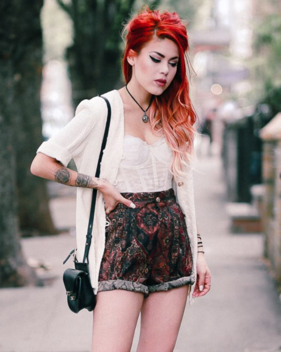 Looks con short vintage;chica rockera pelirroja con tatuajes de flores en los brazos, cosré blanco y short con estampado retro, suéter tejido y bolsa negra