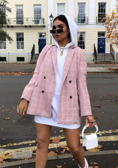 Looks con sudadera; mujer caminando en la calle con hoodie blanco como vestido, saco rosa con cuadtros, bolsa pequeña blanca y lentes de sol rectangulares