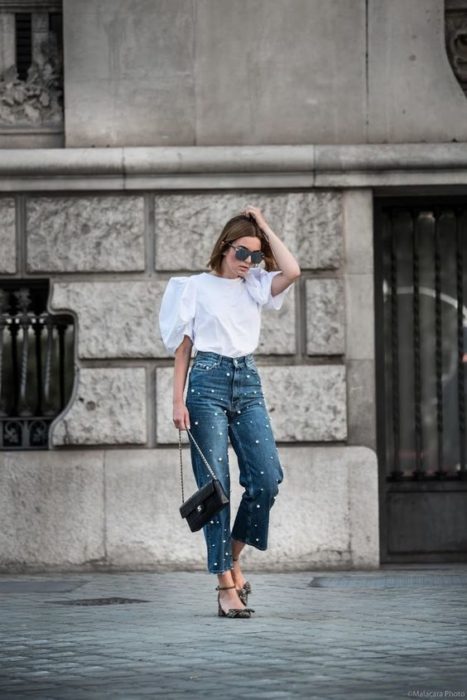 Mujer posando con blusa blanca y jeans con aplicaciones de perlas