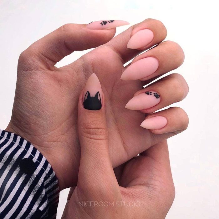 Manicura en tono rosa pastel en forma de almendra con decorado de gatos en negro