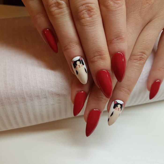 Manicura en tonos rojo con estilo almendra decorado con stickers de gato