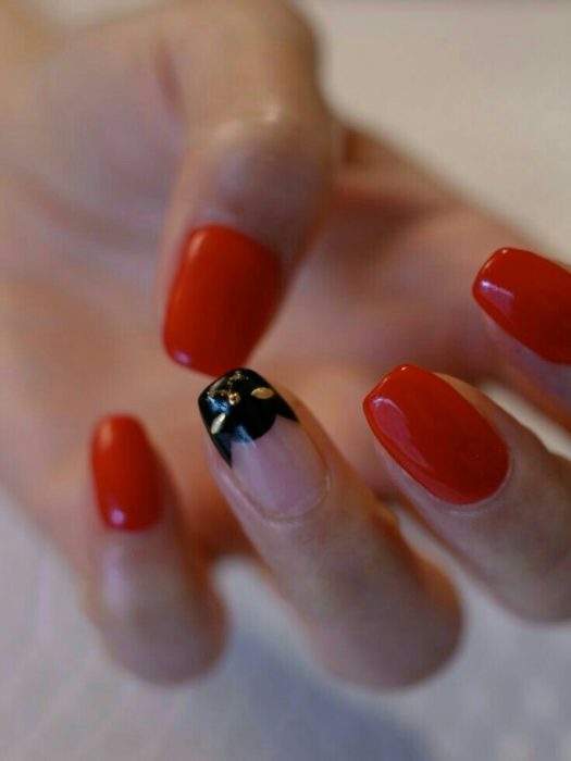 Manicura en tono rojo cereza con decorado de silueta de gato en negro y dorado