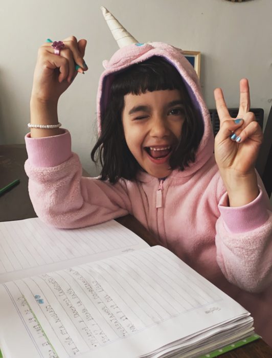 Niña llamada Angostina usando una sudadera de unicornio mientras está haciendo su tarea 