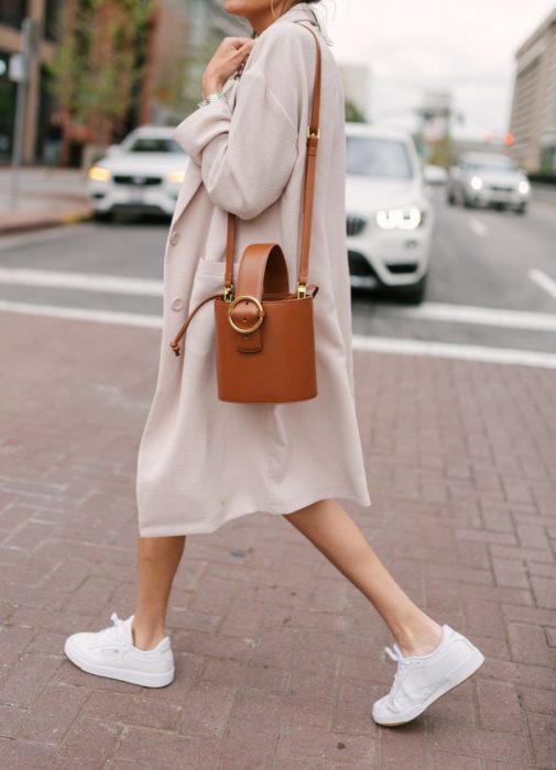 Chica usando tenis blancos, con un blazer largo y bucket bag color camel