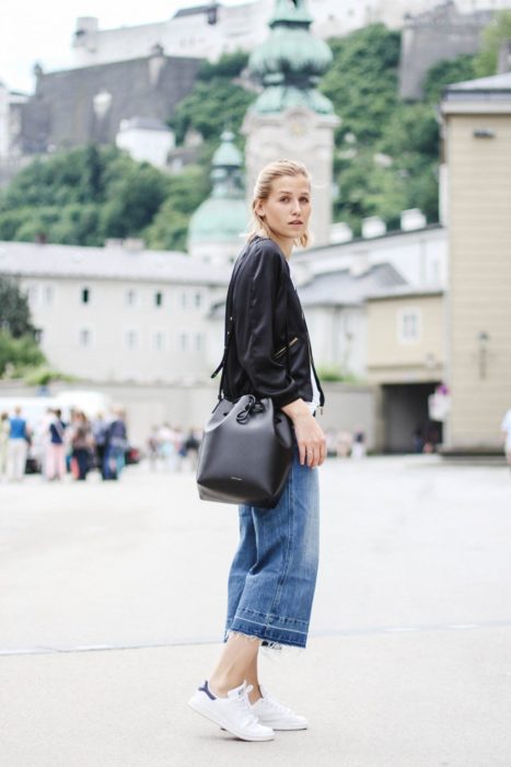 Chica usando tenis blancos, mom jeans, camisa negra y bucket bag color negro