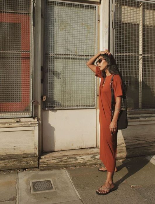 Mujer se toca el cabello y usa vestido naranja larga y flip flops