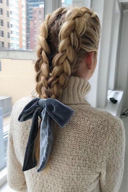 Chica rubia con trenzas alemanas amarradas con moño azul de terciopelo