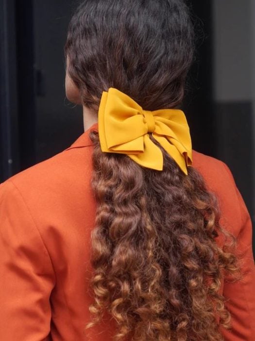 Chca rizada de cabello largo con moño amarillo en una coleta