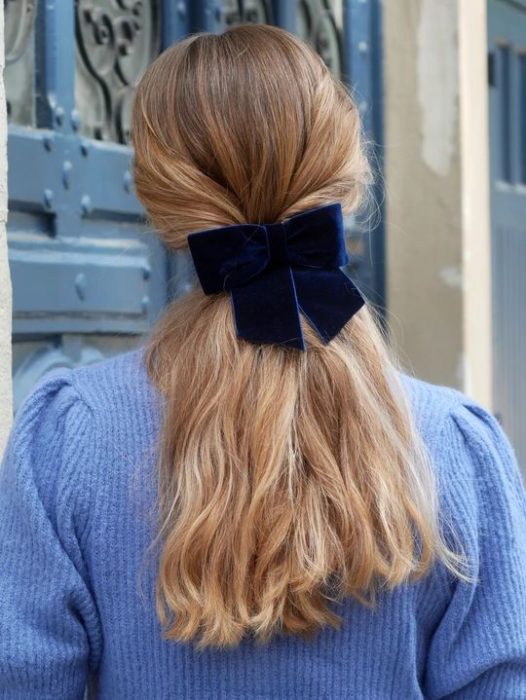 Chica rubia de cabello largo con coleta baja con moño negro