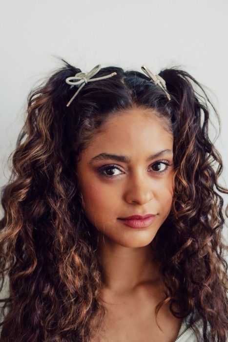 Chica de cabello rizado con dos colitas delanteras decoradas con listones blancos