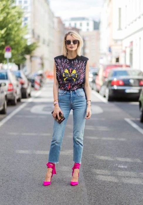 Chica rubia de cabello corto con jean y blusa negra sin mangas con estampado de banda de rock