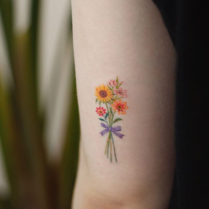 Tatuaje de flores en el brazo, es un ramo de flores atado con un listón morado