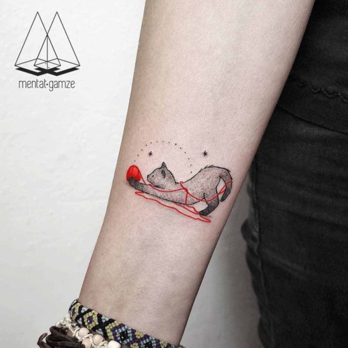 Tatuajes de gatos; tatuaje en el brazo de felino gris jugando con bola de estambre roja