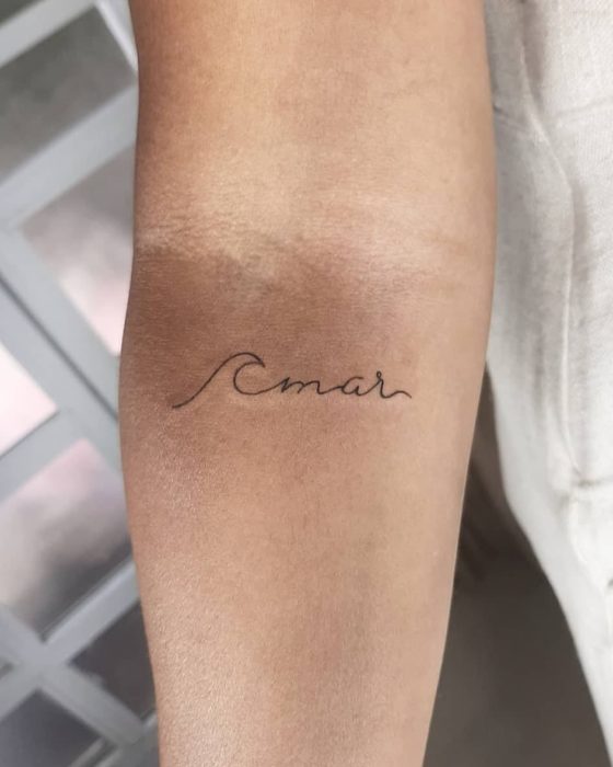 Tatuaje minimalista de la palabra mar junto a una ola