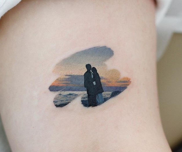 Tatuaje en tonos cálidos de una pareja admirando el atardecer en la playa