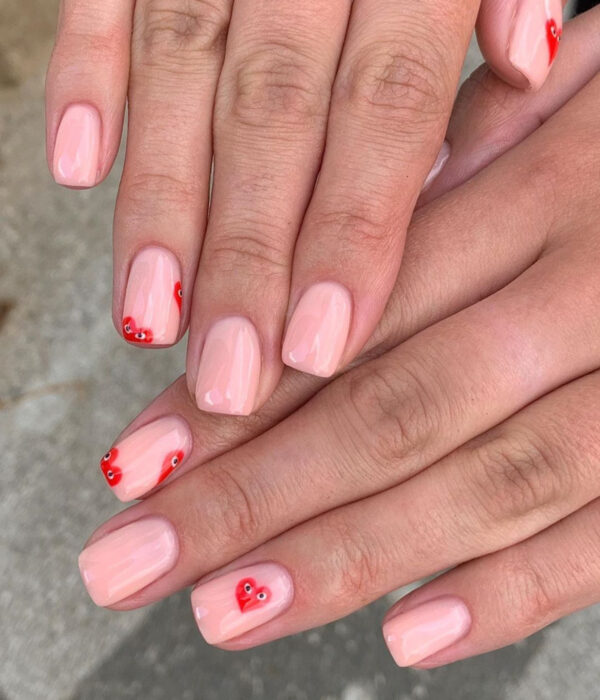 Diseño de manicure sencillos, femeninos y naturales; uñas cortas cuadradas pintadas con esmalte nude rosa y dibujos de corazones rojos con ojos