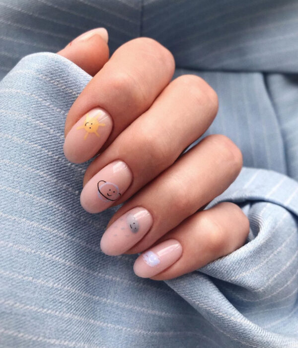 Diseño de manicure sencillos, femeninos y naturales; uñas largas redondas pintadas con esmalte nude y dibujos de Sol, planeta Saturno y nube gris con lluvia y caritas felices