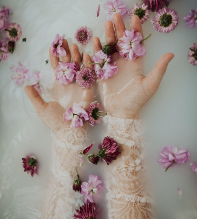 Milk bath; fotografía de manos de mujer en el agua con leche y flores mroadas