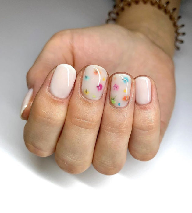 Diseños de manicura milk bath; uñas cortas color blanco con clores pequeñas azules, amarillas, anaranjadas, verdes y rosas