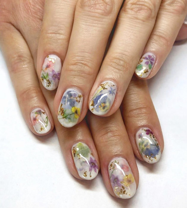 Diseños de manicura milk bath; uñas cortas color blanco con flores azules, amarillas y moradas