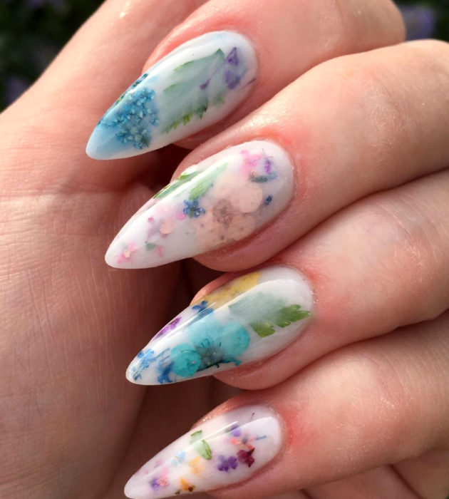 Diseños de manicura milk bath; uñas largas stiletto, blancas con flores azules, rosas, amarillas y moradas