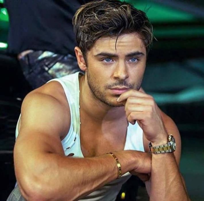 Zac Efron usando camisa sin mangas y una mano en su barbilla