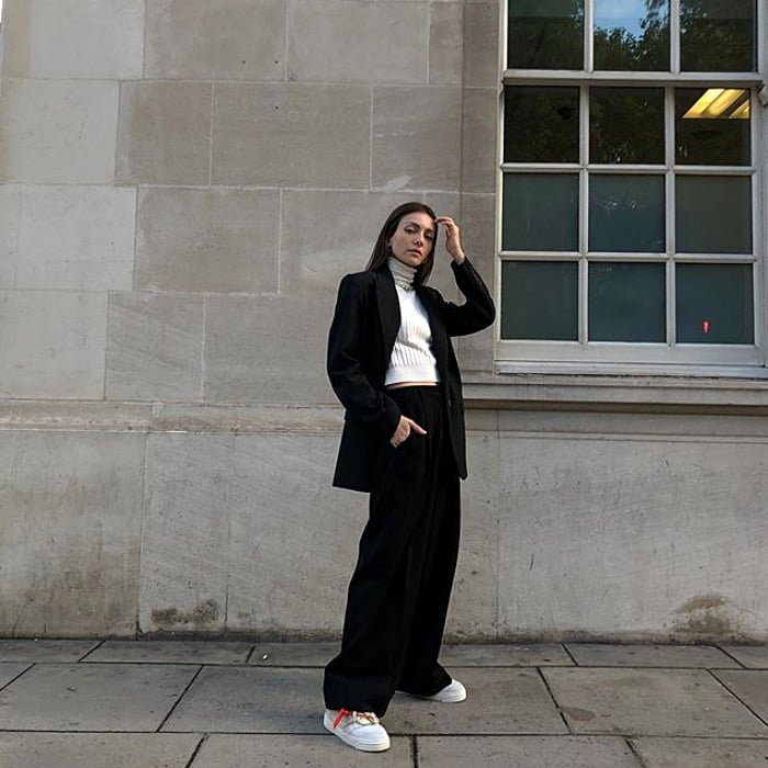 chica de cabello castaño con top blanco de cuello alto, blazer negro y pantalones negros de vestir, tenis deportivos