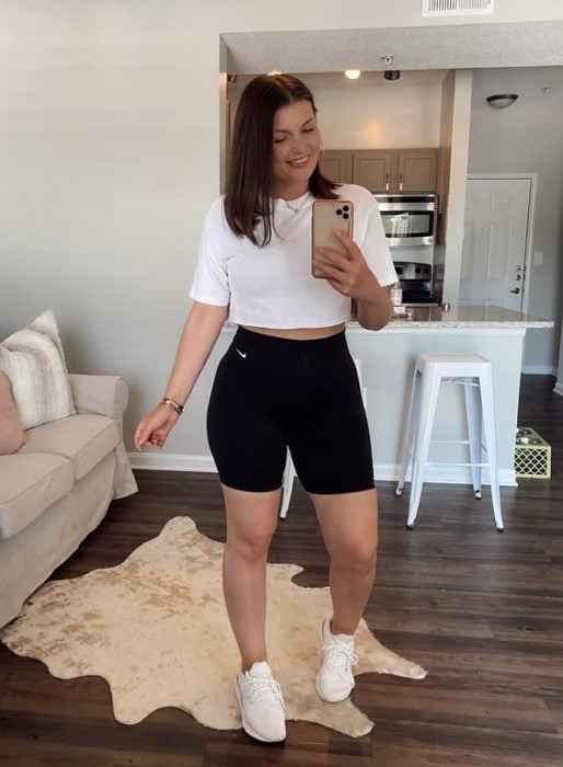 Chica se toma selfie frente al espejo con blusa blanca y shorts negros de ciclista