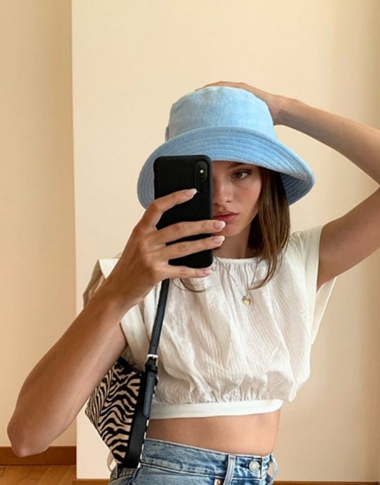 chica de cabello castaño usando un bucket hat azul claro, blusa blaca de manga corta y bolso pequeño de cebra 