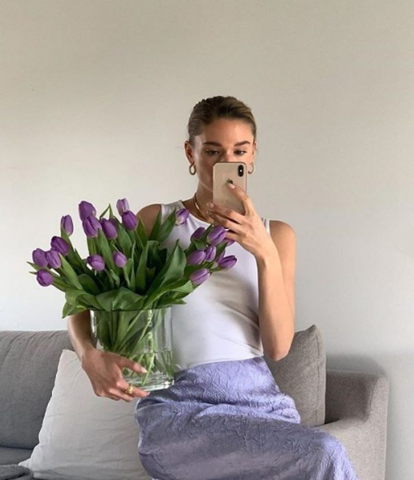 chica con flores moradas usando un top lila y falda de satén morada