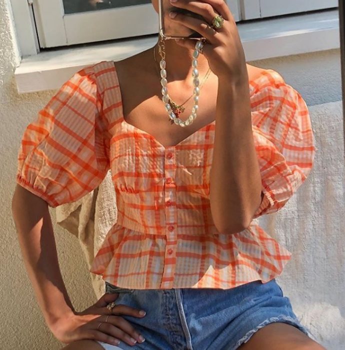 chica morena usando una blusa anaranjada claro con shorts de mezclilla y collar de piedritas blancas