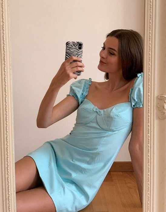 chica de cabello castaño usando un vestido corto en color azul pastel baby blue enfrente de un espejo