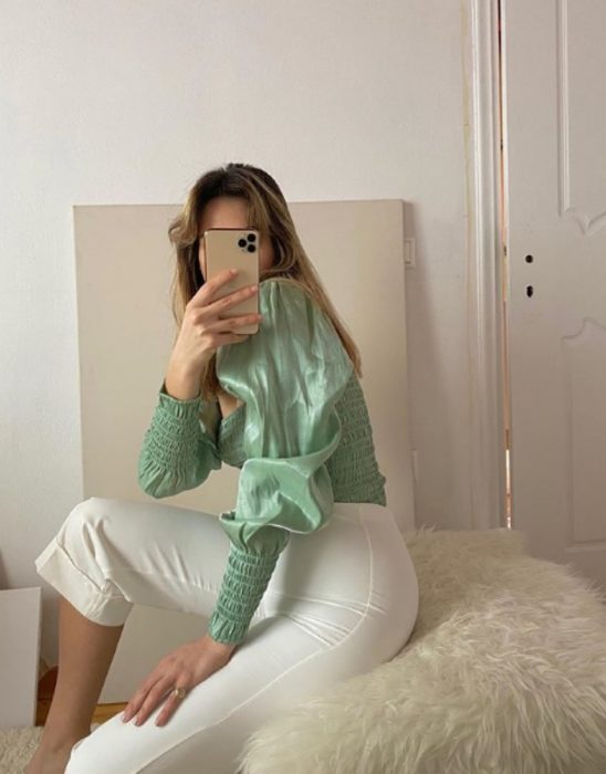 chica tomandose un selfie usando una blusa de manga larga en color pistache o verde menta con pantalones cortos blancos