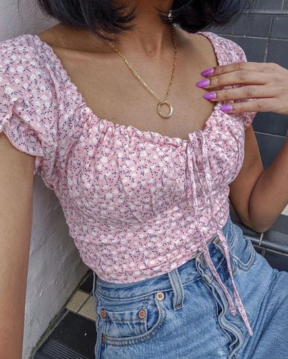 chica usando una blusa de manga corta con estampado de flores blancas y fondo rosa pastel con un collar de planta