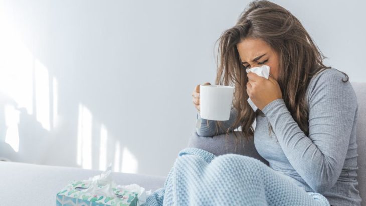 Chica enferma de gripa, tomando té y sonándose la nariz