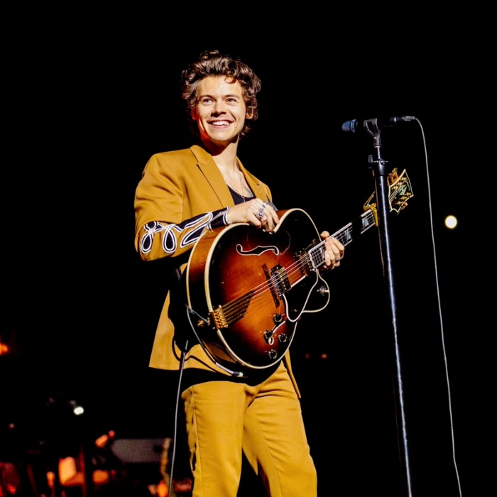 harry styles en traje amarillo con guitarra