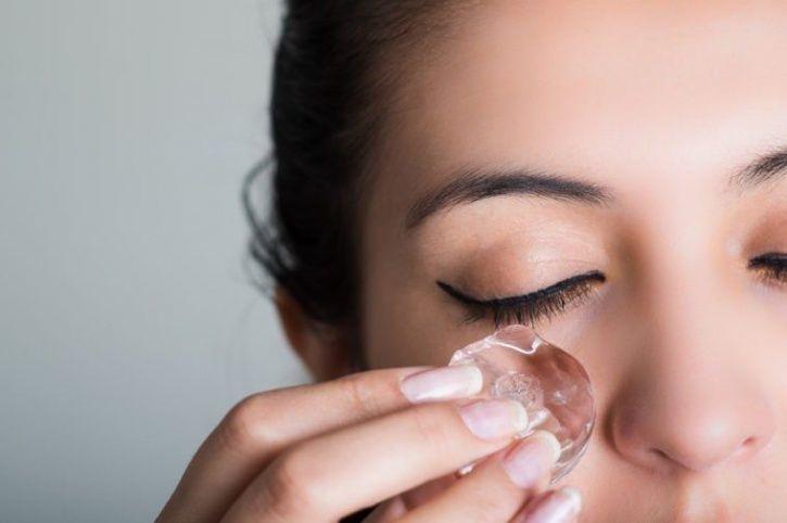 Chica frotando un hielo sobre sus ojos